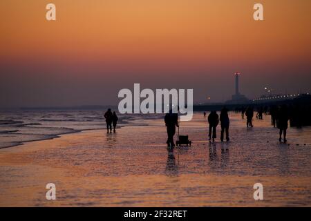 Brighton et la plage de Hove à marée basse, en regardant vers l'ouest. Silhouettes de personnes marchant le long de la rive au coucher du soleil. Pêcheur collectant des vers pour pêcher des appâts. Sussex, Angleterre. Banque D'Images