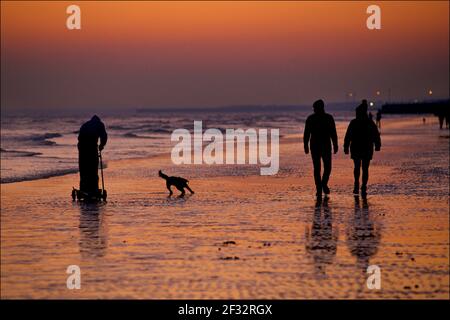 Brighton et la plage de Hove à marée basse, en regardant vers l'ouest. Silhouettes de personnes marchant le long de la rive au coucher du soleil. Pêcheur collectant des vers pour pêcher des appâts. Sussex, Angleterre. Banque D'Images