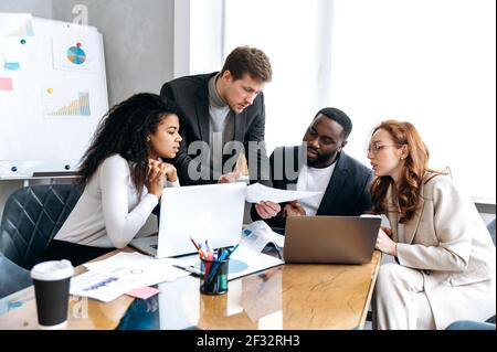 Équipe d'affaires multiraciale sur le briefing, discutant des idées pour le nouveau démarrage ou projet. Des collègues sérieux et élégants travaillant ensemble dans un bureau moderne, regardant les documents, apprenant les rapports financiers Banque D'Images