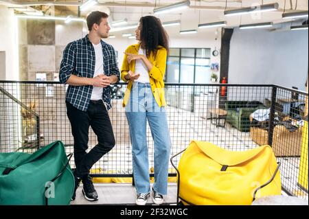 Des amis élégants collègues ou étudiants ayant une conversation, debout dans un bureau moderne. Jeunes collègues multiethniques adultes qui parlent de projet d'entreprise, de travail ou de questions d'étude Banque D'Images