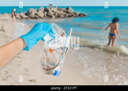La main d'un homme dans des gants de protection en latex tient un sac de déchets contre la mer. Nettoyer les ordures derrière les gens. Banque D'Images