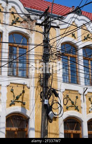 Enchevêtrement de fils électriques sur le poteau contre le bâtiment traditionnel. Réseau complexe d'au-dessus du sol en Roumanie Banque D'Images