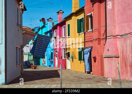 Vue sur la rue avec façades colorées de maisons et buanderie suspendue le jour du printemps avec ciel bleu dans la célèbre île de Burano, Italie. Banque D'Images