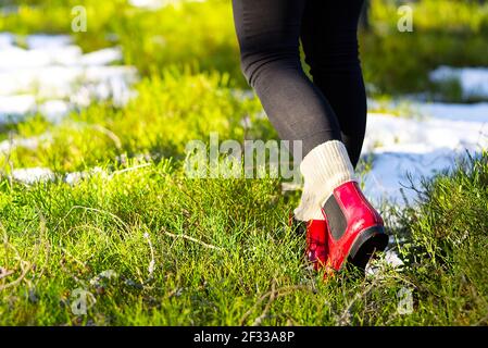 Concept automne ou printemps avec forêt colorée et bottes de pluie à l'extérieur. Gros plan des pieds de femme marchant dans des bottes rouges. Banque D'Images