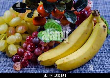 Encore la vie avec des bananes, des raisins et des mandarines décoratives. Baies et fruits en gros plan sur fond blanc et bleu. Nourriture, ingrédients. Vue latérale Banque D'Images