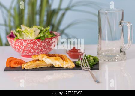 Demi-sandwich grillé sur un plateau en ardoise avec une salade hors foyer et un verre à bière vide. Mise au point sélective et gros plan. Concept de nourriture et de style de vie. Banque D'Images