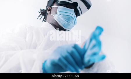 Médecin noir afro-américain en uniforme de protection et avec des lunettes VR mettant des gants. Photo de haute qualité Banque D'Images