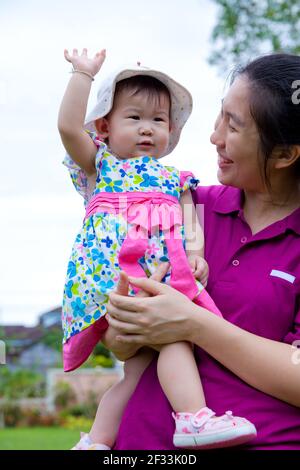 Une femme asiatique heureuse et une petite fille mignonne se détendant à la maison arrière cour et ciel lumineux fond, mère transportant sa fille Banque D'Images