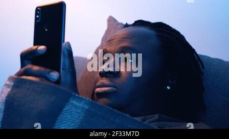 Afro-américain fatigué noir homme tenant smartphone tout en étant allongé sur le canapé . Photo de haute qualité Banque D'Images