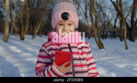 Enfant fille blogueur faisant appel vidéo sur téléphone mobile, selfie photo pour le réseau social parc d'hiver Banque D'Images
