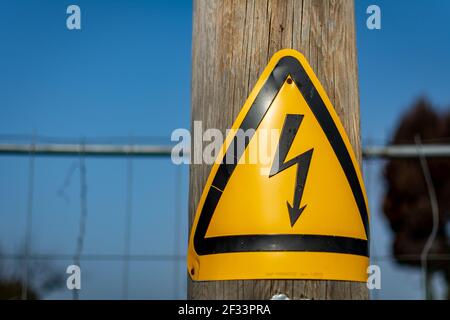 Panneau au bas d'un poteau électrique en bois d'avertissement du danger d'électrocution si une tentative est faite pour monter le poteau à côté d'une rue. Banque D'Images