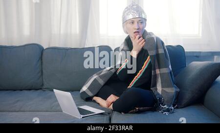 Une jeune femme craintive avec un chapeau en aluminium parcourant les médias sociaux. Théorie de la conspiration autour de 5g réseau détruisant le cerveau. Photo de haute qualité Banque D'Images