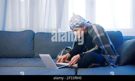 Une jeune femme craintive avec un chapeau en aluminium parcourant les médias sociaux. Théorie de la conspiration autour de 5g réseau détruisant le cerveau. Photo de haute qualité Banque D'Images