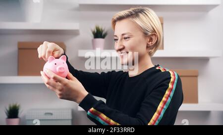Portrait d'une jeune femme caucasienne heureuse mettant des pièces de monnaie dans la banque de piggy. Photo de haute qualité Banque D'Images