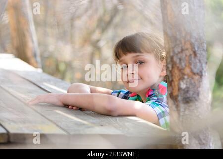 Une jeune fille de dix ans est assise à une table en bois dans le forêt et heureusement regardé dans le cadre Banque D'Images