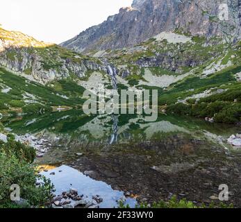 Lac de Velicke pleso et chute de vodopad de Velicky à Velicka dolina vallée avec des sommets et le reflet du ciel en automne Vysoke Tatry Montagnes en Slovaquie Banque D'Images