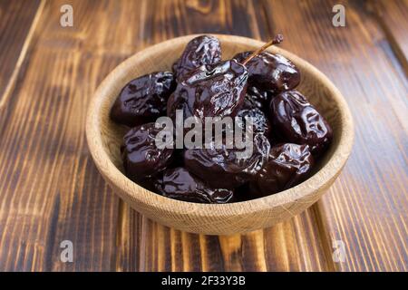 Prunes marinées dans le bol brun sur fond de bois. Produit fermenté. Banque D'Images