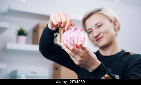 Portrait d'une jeune femme caucasienne heureuse mettant des pièces de monnaie dans la banque de piggy. Photo de haute qualité Banque D'Images