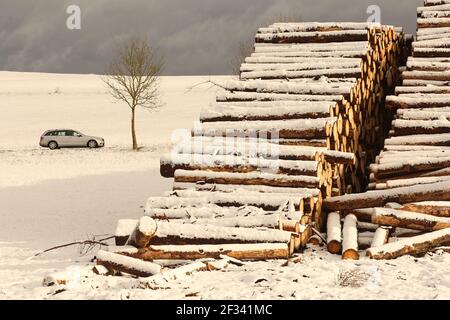 Elbingerode, Allemagne. 15 mars 2021. La neige se trouve sur un tas de bois entreposé au bord d'une forêt dans les montagnes Harz près d'Elbingerode, derrière elle une voiture conduit le long d'une route. Les premières chutes de neige ont commencé dans la nuit jusqu'à lundi. Le temps frais de l'hiver se poursuivra dans les jours à venir. Credit: Matthias Bein/dpa-Zentralbild/dpa/Alay Live News Banque D'Images