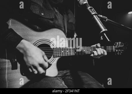 Le guitariste joue une guitare acoustique avec un capo devant un microphone. Le concept d'enregistrement de musique, de répétition ou de spectacle en direct. Banque D'Images