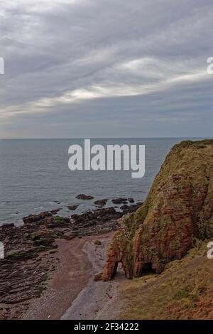 L'arche de mer au-dessous de la pointe Maw Skelly et les falaises de la mer sur et au-dessus de la plage étroite de Shingle avec les affleurements rocheux exposés par une marée basse. Banque D'Images