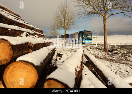 Elbingerode, Allemagne. 15 mars 2021. La neige se trouve sur une pile de bois stockée au bord d'une forêt dans les montagnes Harz près d'Elbingerode, avec un bus qui roule sur une route derrière elle. Les premières chutes de neige ont commencé dans la nuit jusqu'à lundi. Le temps frais de l'hiver se poursuivra dans les jours à venir. Credit: Matthias Bein/dpa-Zentralbild/dpa/Alay Live News Banque D'Images