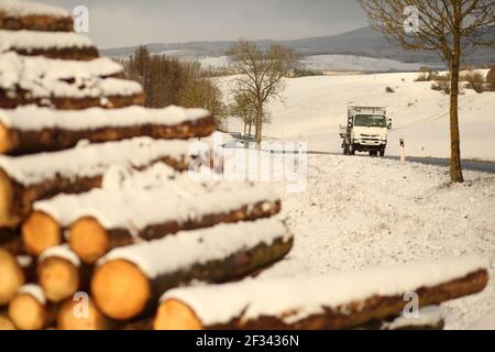 Elbingerode, Allemagne. 15 mars 2021. La neige se trouve sur une pile de bois stockée au bord d'une forêt dans les montagnes Harz près d'Elbingerode, avec un véhicule roulant sur une route derrière elle. Les premières chutes de neige ont commencé dans la nuit jusqu'à lundi. Le temps frais de l'hiver se poursuivra dans les jours à venir. Credit: Matthias Bein/dpa-Zentralbild/ZB/dpa/Alay Live News Banque D'Images