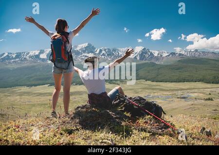 Un couple heureux de jeunes randonneurs se tient debout avec les bras levés sur fond de montagnes enneigées Banque D'Images