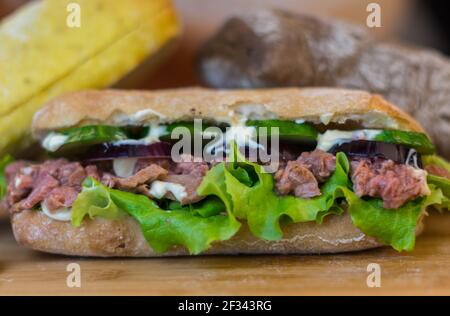 Sandwich au thon, avec des oignons rouges, des tranches de sallad et de concombre, se déplaçant sur une table en bois Banque D'Images