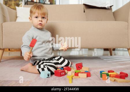 Portrait d'un enfant regardant l'appareil photo lorsqu'il est assis sur le et jouer avec des jouets éducatifs dans la chambre Banque D'Images