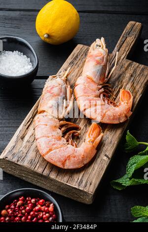 Crevettes de mer sur une planche en bois avec des ingrédients sur une table en bois noir, photo de nourriture. Banque D'Images