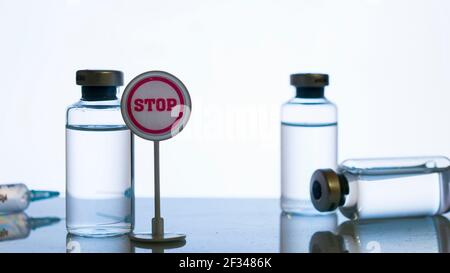 Concept d'effet secondaire du vaccin : un panneau d'arrêt à côté d'un flacon et une silhouette de seringue sur une surface réfléchissante Banque D'Images