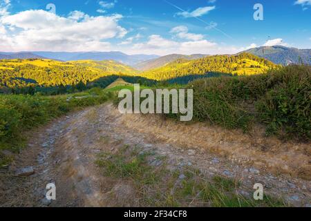 paysage rural dans les montagnes au lever du soleil d'été. route de campagne à travers des pâturages herbeux se déroulant dans la vallée éloignée. nuages sur le ciel bleu abov Banque D'Images