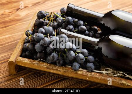 Composition de deux bouteilles de vin rouge sur une table en bois brun. Bouteilles de vin rouge en boîte sur des raisins mûrs noirs sur une table en bois. Vin de collection ancien Banque D'Images
