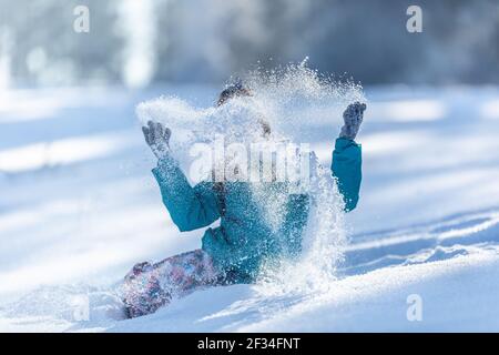 Un enfant jette de la neige en poudre dans l'air assis sur de la neige fraîche au sol. Banque D'Images