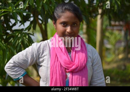 Gros plan d'une adolescente bengali indienne vêtue de coton blanc salwar avec dhupatta rose debout devant un manguier, concentration sélective Banque D'Images