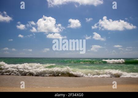 de fortes vagues sur une belle plage de sable avec un ciel bleu nuageux. Banque D'Images