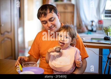 adorable tout-petit aime manger de la glace à la popsicle sur les genoux de ses parents dans l'intérieur de la maison Banque D'Images