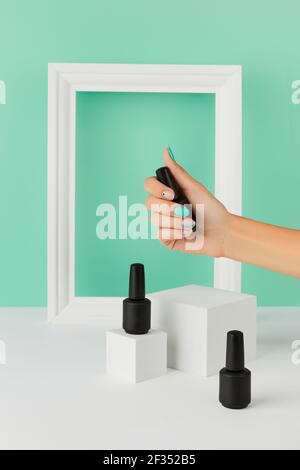 Les femmes tiennent main une bouteille de vernis à ongles sur fond turquoise Banque D'Images