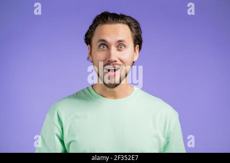 L'homme dépeint l'étonnement, montre l'effet visage émerveillement de WOW. Surprise excitée gars heureux. Beau modèle mâle choqué sur fond violet. Banque D'Images