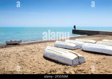 Bateaux à rames sur la rive sablonneuse du lac Michigan avec un couple sur un quai en béton qui donne sur le lac. Banque D'Images