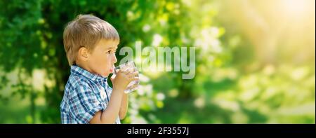 Joli garçon buvant un verre d'eau pure dans la nature. Banque D'Images