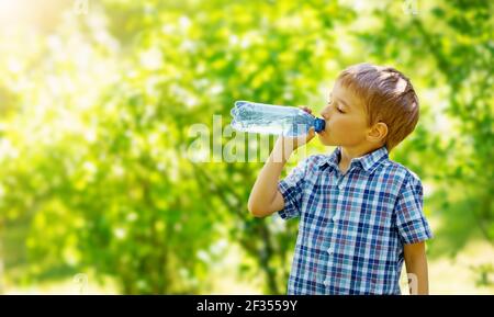 Joli garçon buvant une bouteille d'eau pure dans la nature. Banque D'Images