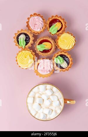 Délicieux petits gâteaux et une tasse de cacao avec guimauves sur fond rose pastel. Banque D'Images