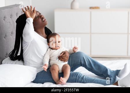 Maman afro-américaine fatiguée assise avec un bébé sur le lit Banque D'Images