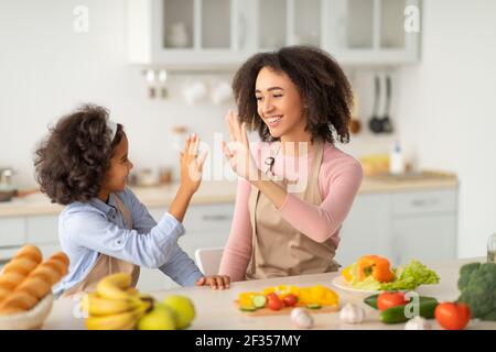 Femme noire donnant cinq élevé à la fille dans la cuisine Banque D'Images