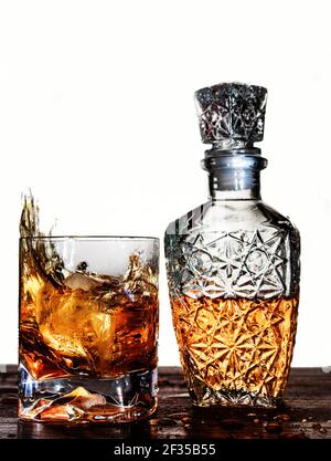 Un cube de glace tombant sur un verre à whisky sur fond blanc éclairé. Journée internationale du whisky Banque D'Images