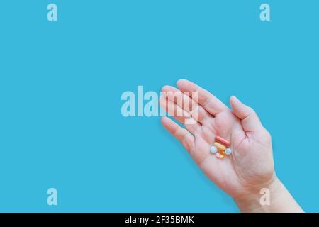 Main de la femme tenant diverses pilules médicales colorées, des comprimés et des capsules. Diverses pilules en main sur fond bleu. Comprimés médicaux dans la paume de la main Banque D'Images