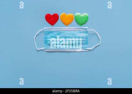 Masque facial de protection et formes de coeur colorées comme feu de circulation sur fond bleu. Masque médical jetable et coeurs. Appréciez les médecins et les infirmières Banque D'Images