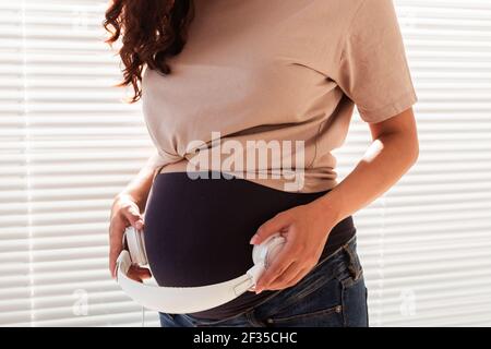 Les mains de la jeune femme enceinte mettent des écouteurs avec de la musique classique sur son ventre. Concept de développement intra-utérin intellectuel de l'enfant Banque D'Images